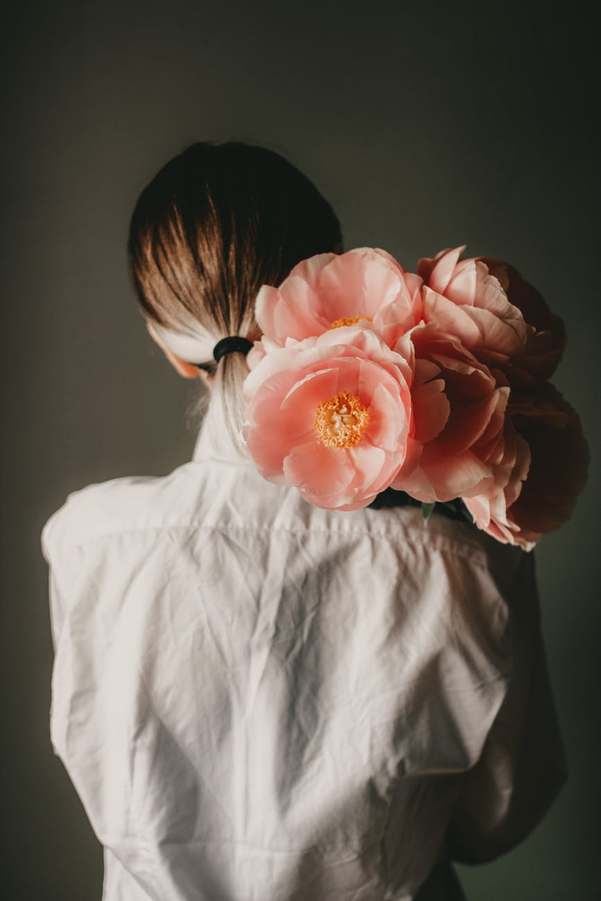 woman standing with bouquet of peonies on shoulder in room