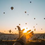 photo of person s hand across flying hot air balloons during golden hour