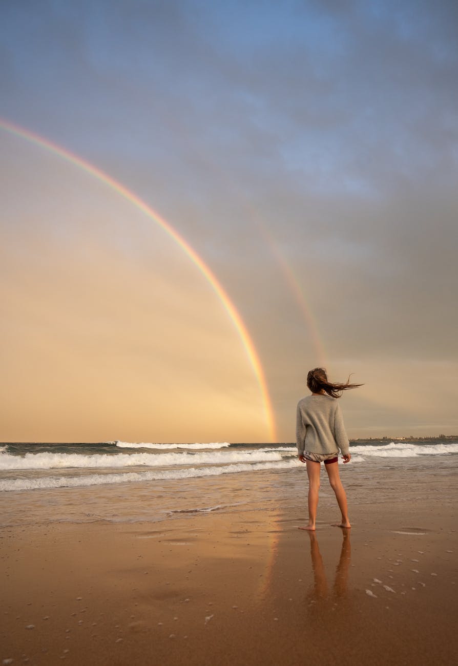 unrecognizable woman standing on shore with rainbow