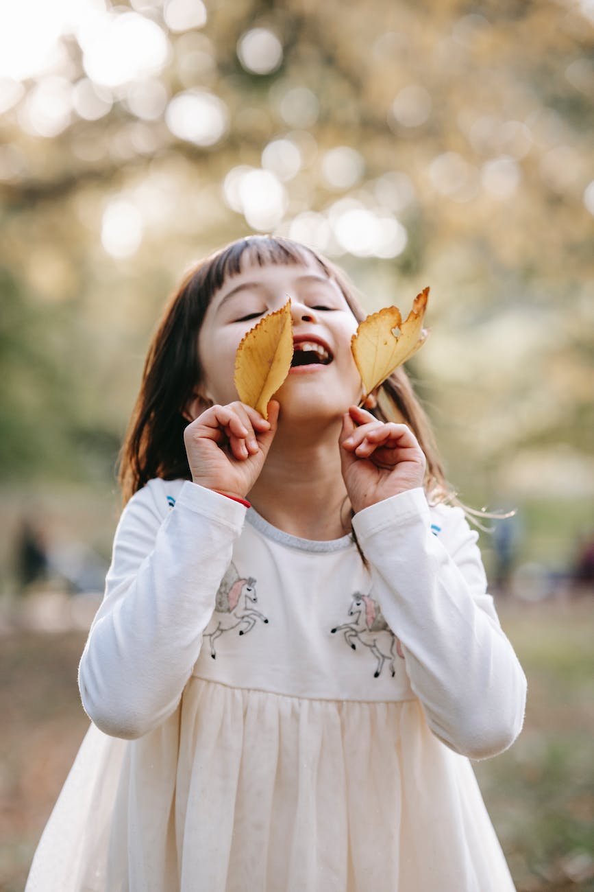 happy little girl with yellow leaves standing in autumn park